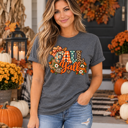 Woman wearing dark heather grey Fall Y'all Texas t-shirt with patchwork cowgirl hat, pumpkins and fall flowers design on a decorated autumn porch
