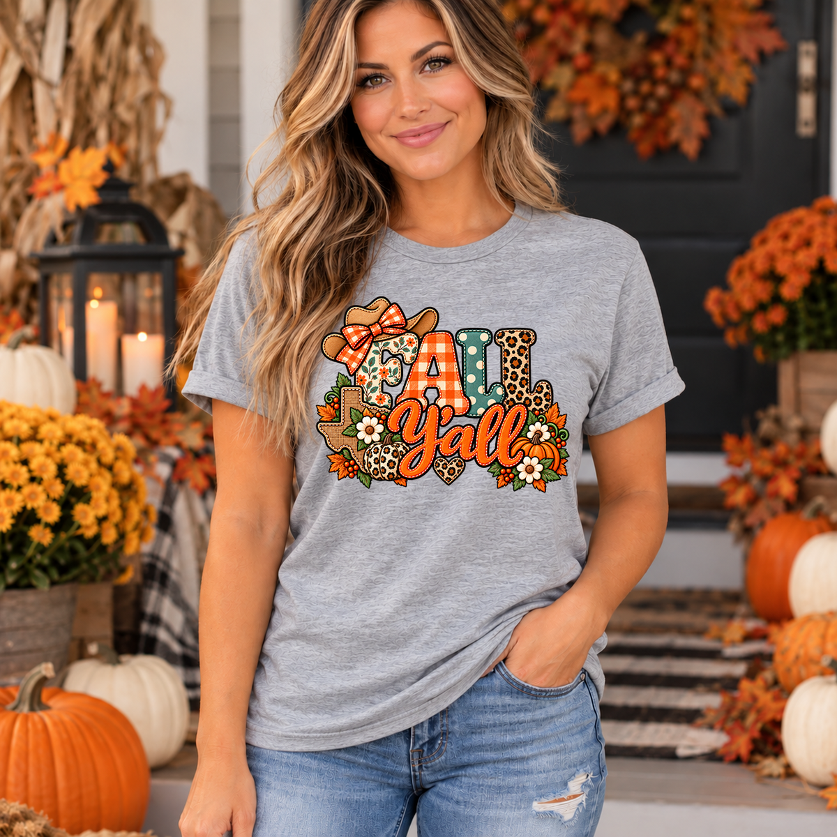 Woman wearing heather grey Fall Y'all Texas t-shirt with patchwork cowgirl hat, pumpkins and fall flowers design on a decorated autumn porch