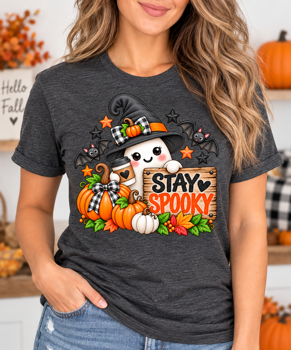 Stay Spooky Halloween t-shirt design featuring a cute ghost in a black witch hat with plaid bow, holding a coffee cup next to a wooden Stay Spooky sign, surrounded by pumpkins, bats, and autumn leaves